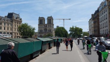 Am Seine-Ufer auf der Straße Quai Saint-Michel mit Blick auf die 2019 durch ein Feuer zerstörte Kirche Notre-Dame. Auf dem abgetrennten Radweg der Einbahnstraße können Radfahrende in beide Richtungen fahren. Die grünen Kisten sind fest installierte Verkaufsbuden für den Bücherflohmarkt.